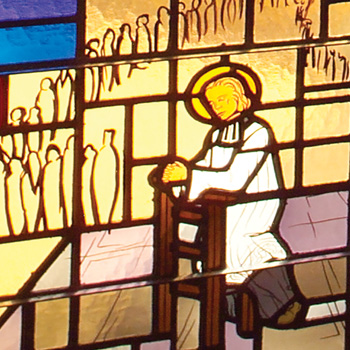 Stained glass window detail of Saint John Vianney in prayer